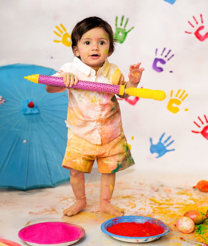 Baby holding a colorful pichkari during a Holi festival-themed photoshoot in Surat studio